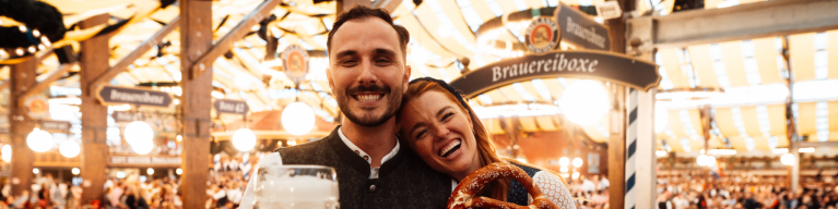 Besucher im Festzelt mit Breze und Maß Oktoberfestbier.